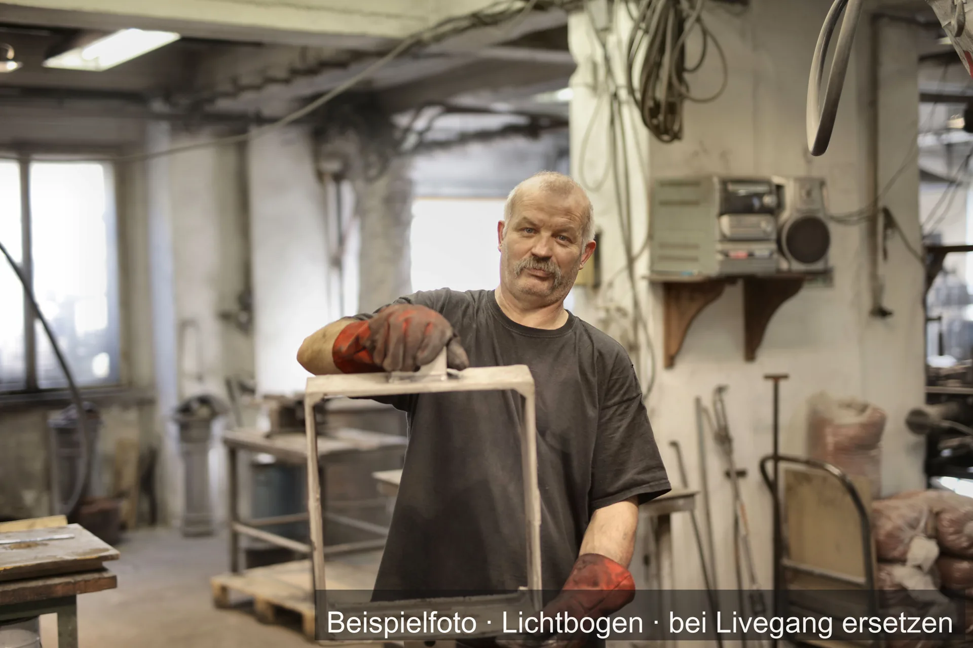 Ein Metallhandwerker mit Arbeitshandschuhen hält ein Werkstück in der Werkstatt.